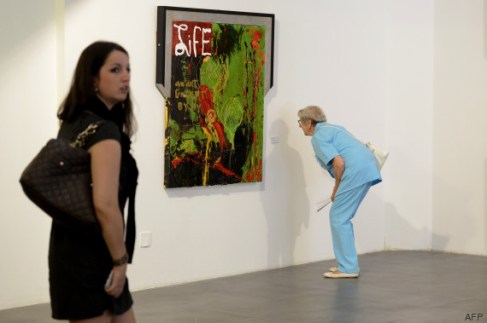 A woman looks a tag beside an artwork at a retrospective of US actor Sylvester Stallone's  paintings entitled "Real Love" Paintings 1975-2015 at the Museum of Contemporary Art in Nice, southeastern France, on May 16, 2015.  AFP PHOTO / FRANCK PENNANT = RESTRICTED TO EDITORIAL USE, MANDATORY MENTION OF THE ARTIST UPON PUBLICATION, TO ILLUSTRATE THE EVENT AS SPECIFIED IN THE CAPTION =